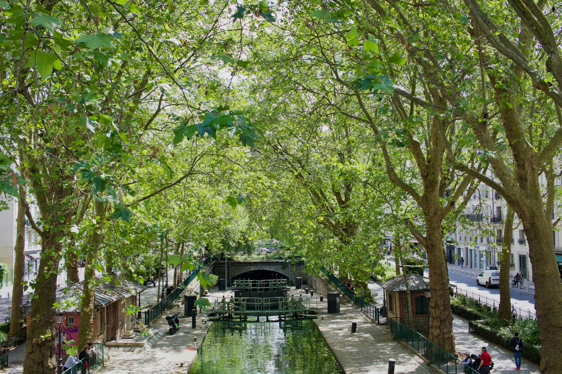 Scenic canal lined with green trees and small riverside structures.